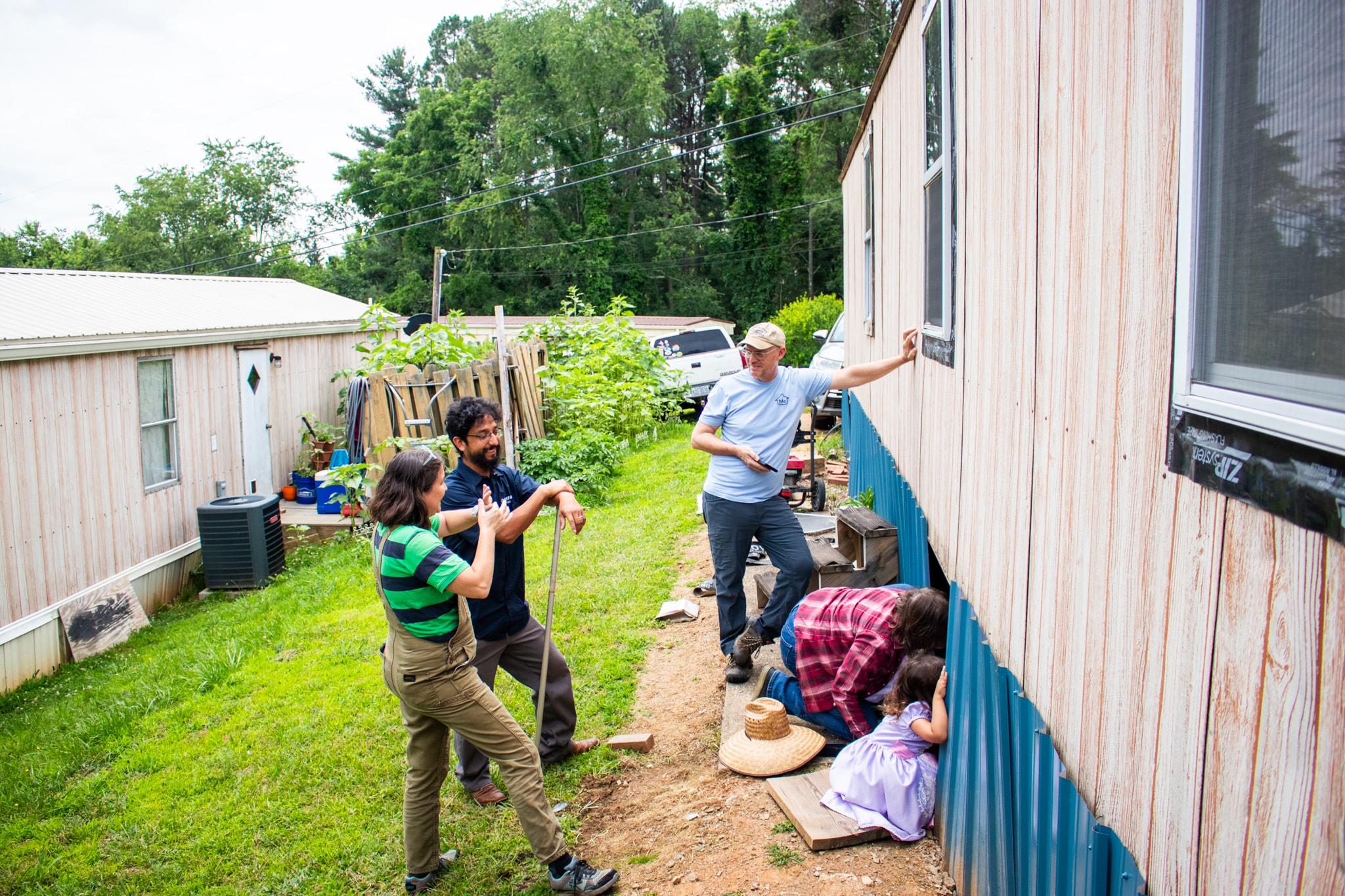 The team—and a small child—peer under the partially removed sheathing of a trailer home.