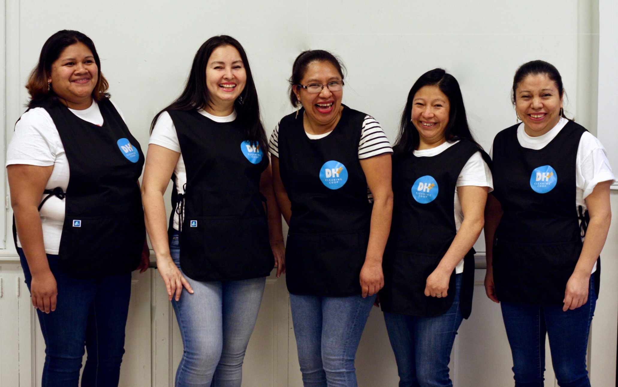 Women in cleaning uniforms pose together, laughing and smiling, wearing cleaning uniforms